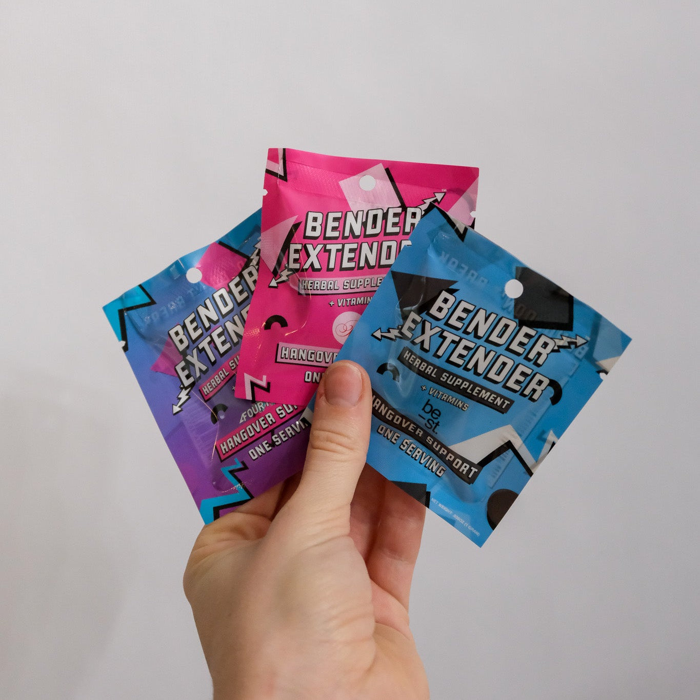 Hand holding three custom 'Bender Extender' supplement packets against a plain background